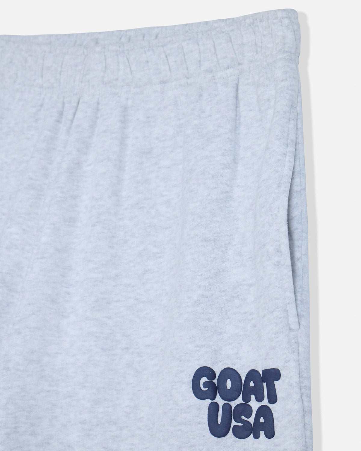 Close-up of light heather gray sweatpants with a navy blue 'GOAT USA' logo printed on the lower left leg.