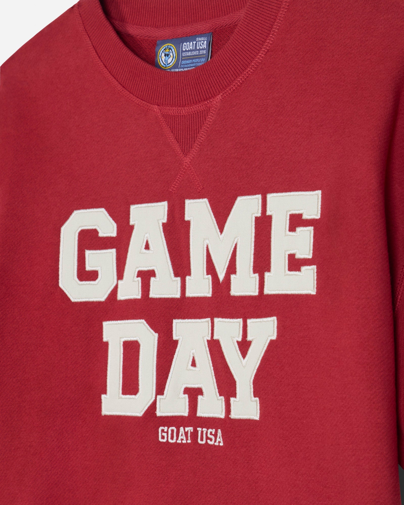 A close-up of a red french terry tee featuring the words 'GAME DAY' in large white varsity-style letters, with 'GOAT USA' printed underneath.#color_tomato