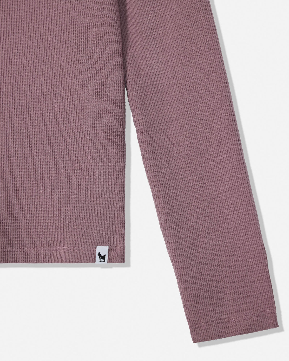 Close-up of a waffle-knit long-sleeve top in dusty mauve pink, showing the sleeve and a small white brand tag with a black dog logo near the hem.