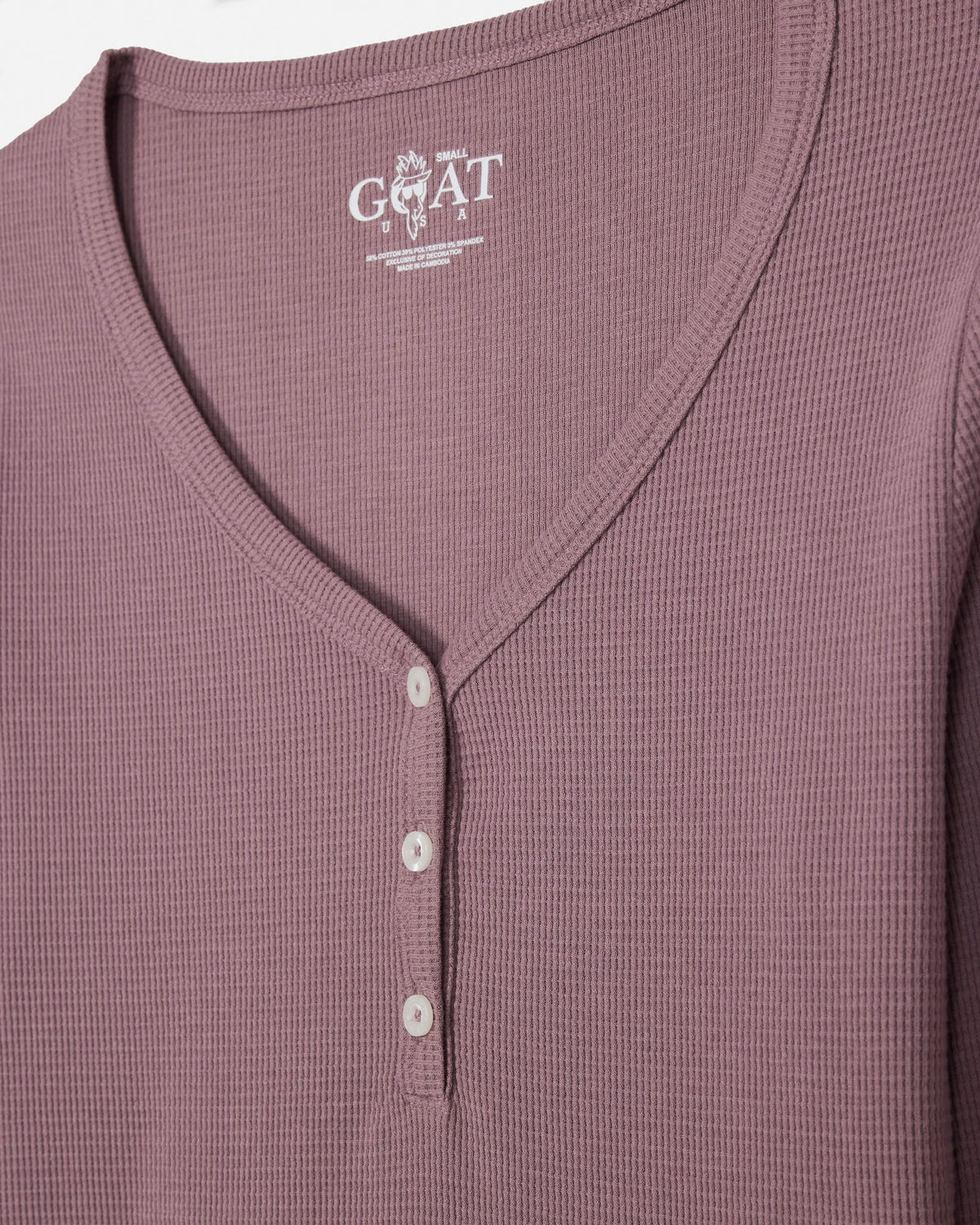 Close-up of a waffle-knit henley top in a muted mauve or dusty rose color, featuring a three-button placket and a visible GOAT USA brand label inside the collar.