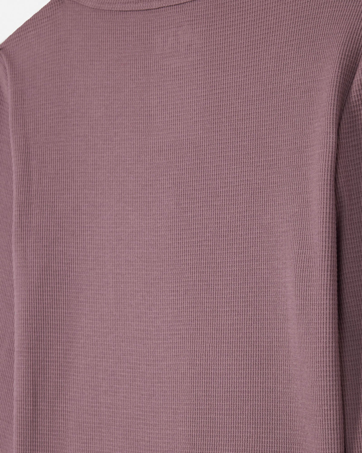 Close-up of a waffle-knit long-sleeve top in a muted dusty mauve or plum color, showing the fine knit texture and a small tonal chest logo.