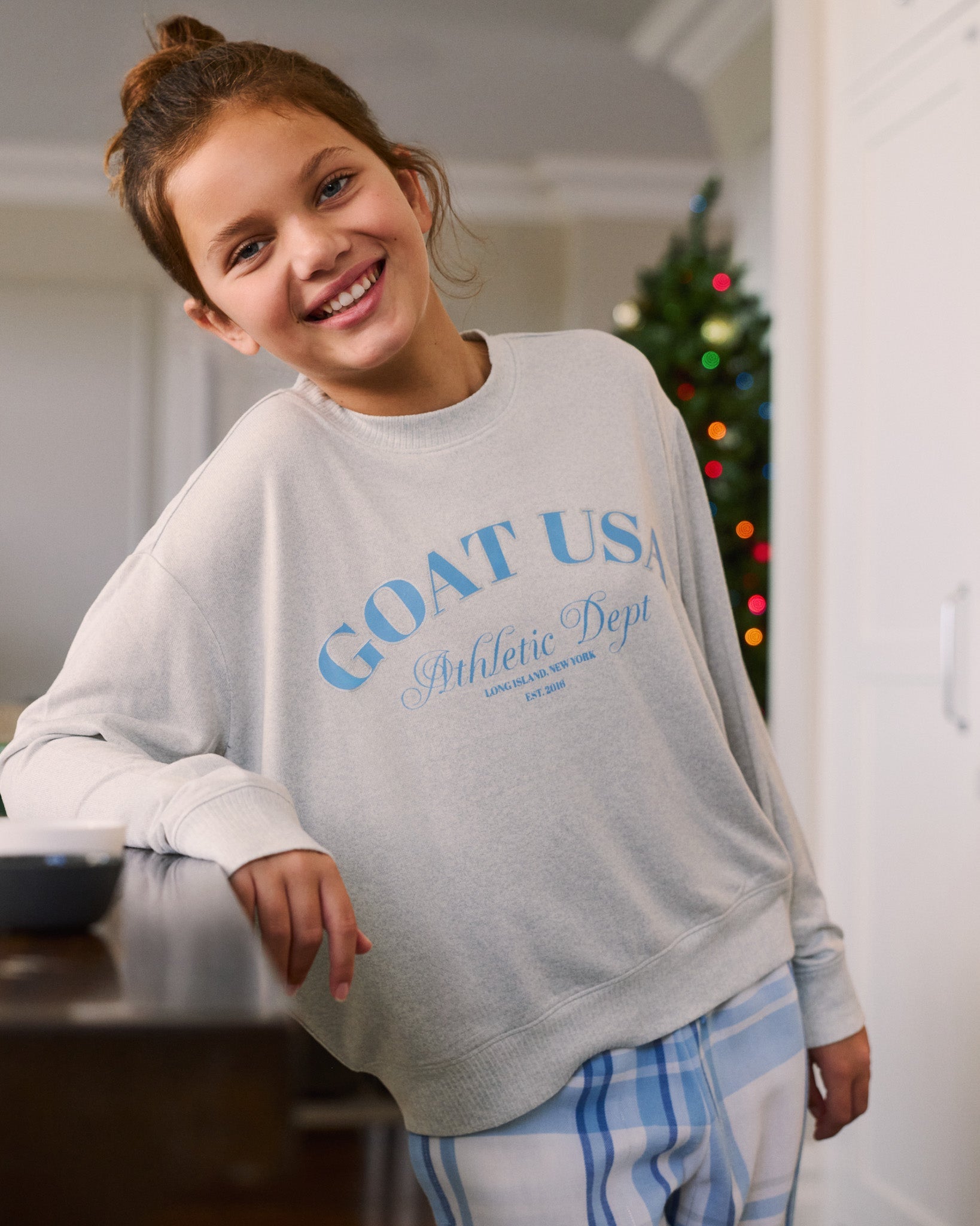 Child wearing a gray sweatshirt with blue text, standing indoors.