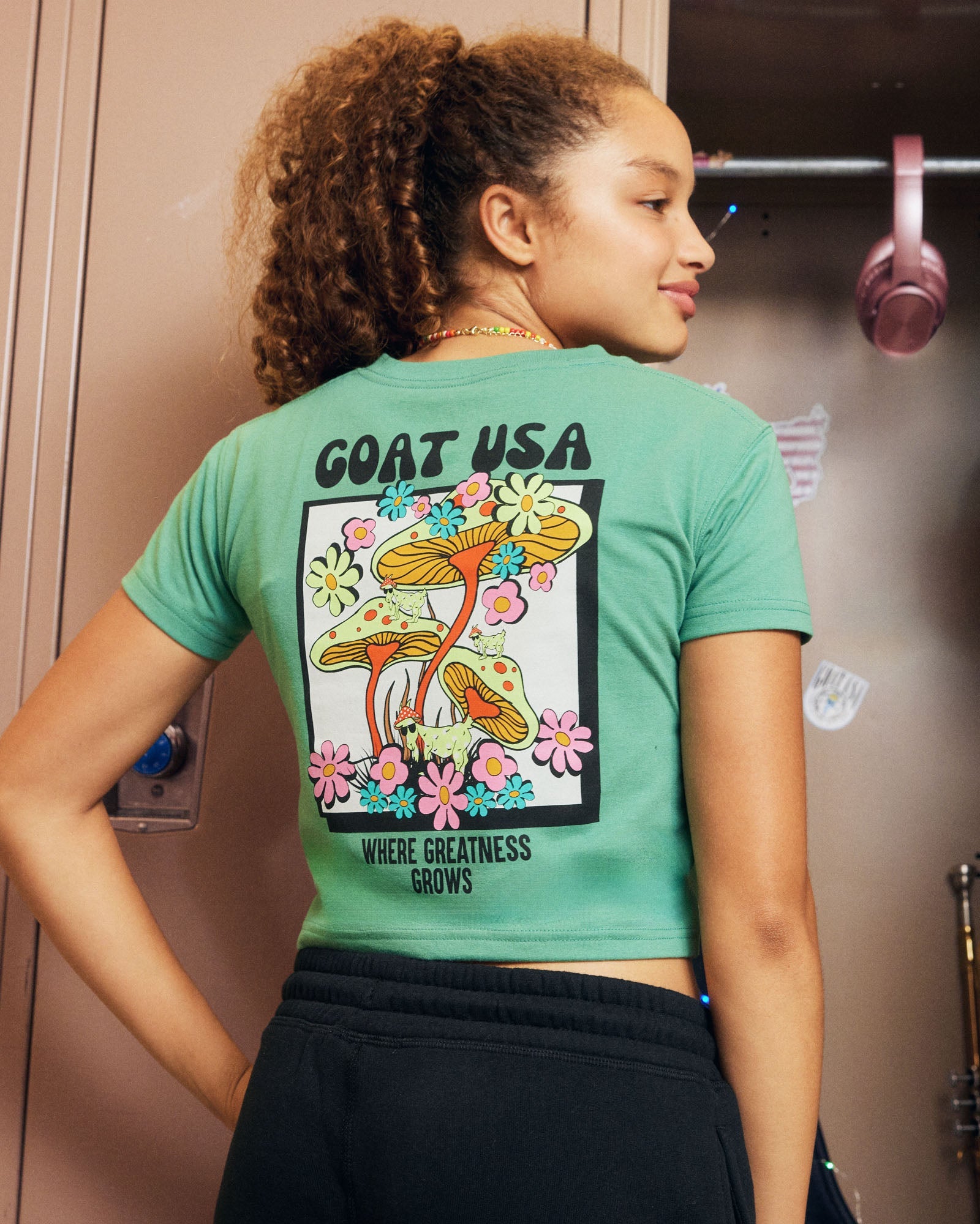 Person wearing a green crop top with a graphic design and text, standing in front of a locker.