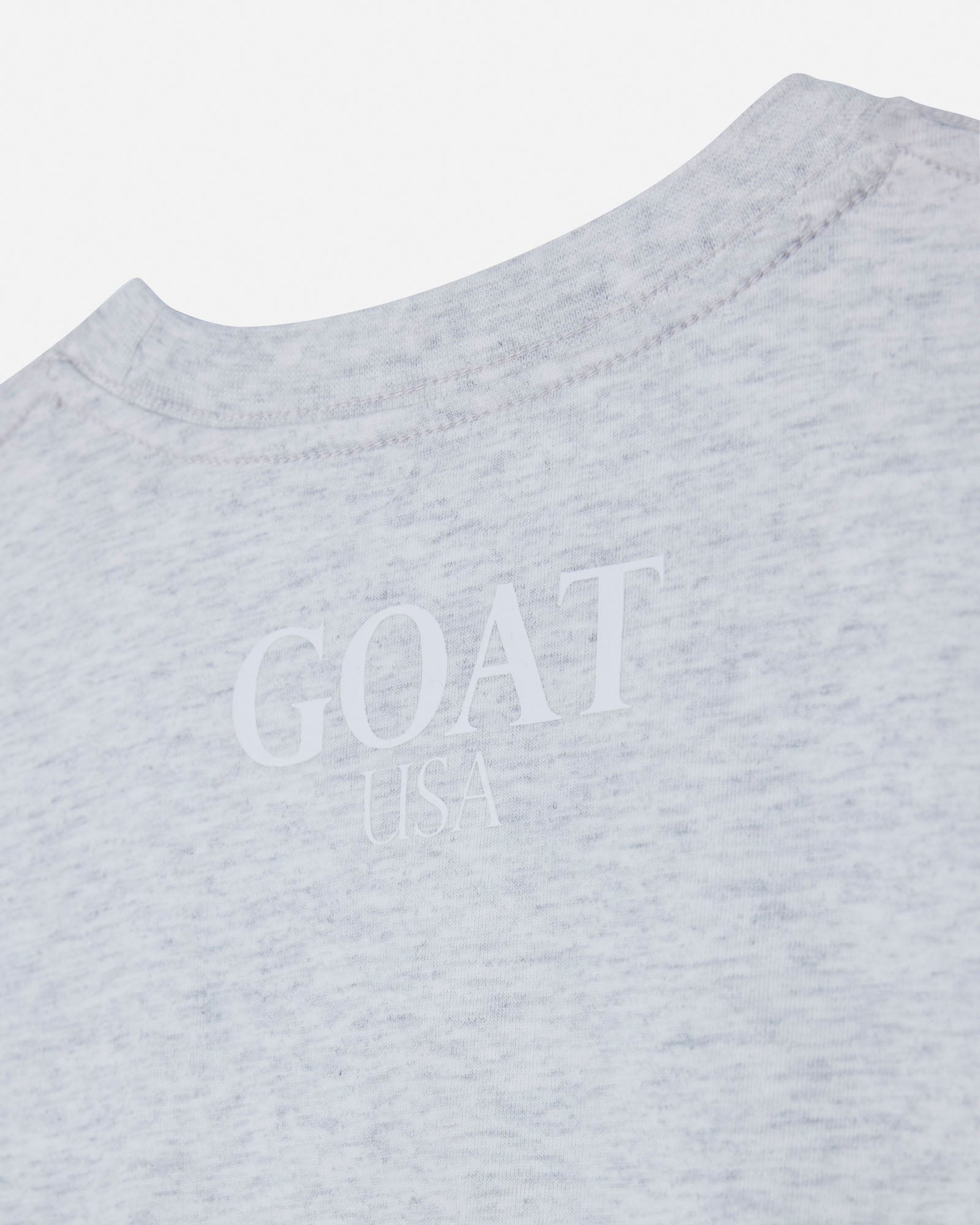Close-up of a light heather gray t-shirt showing the inner collar and a subtle tonal 'GOAT USA' logo printed on the chest.#color_pale-gray