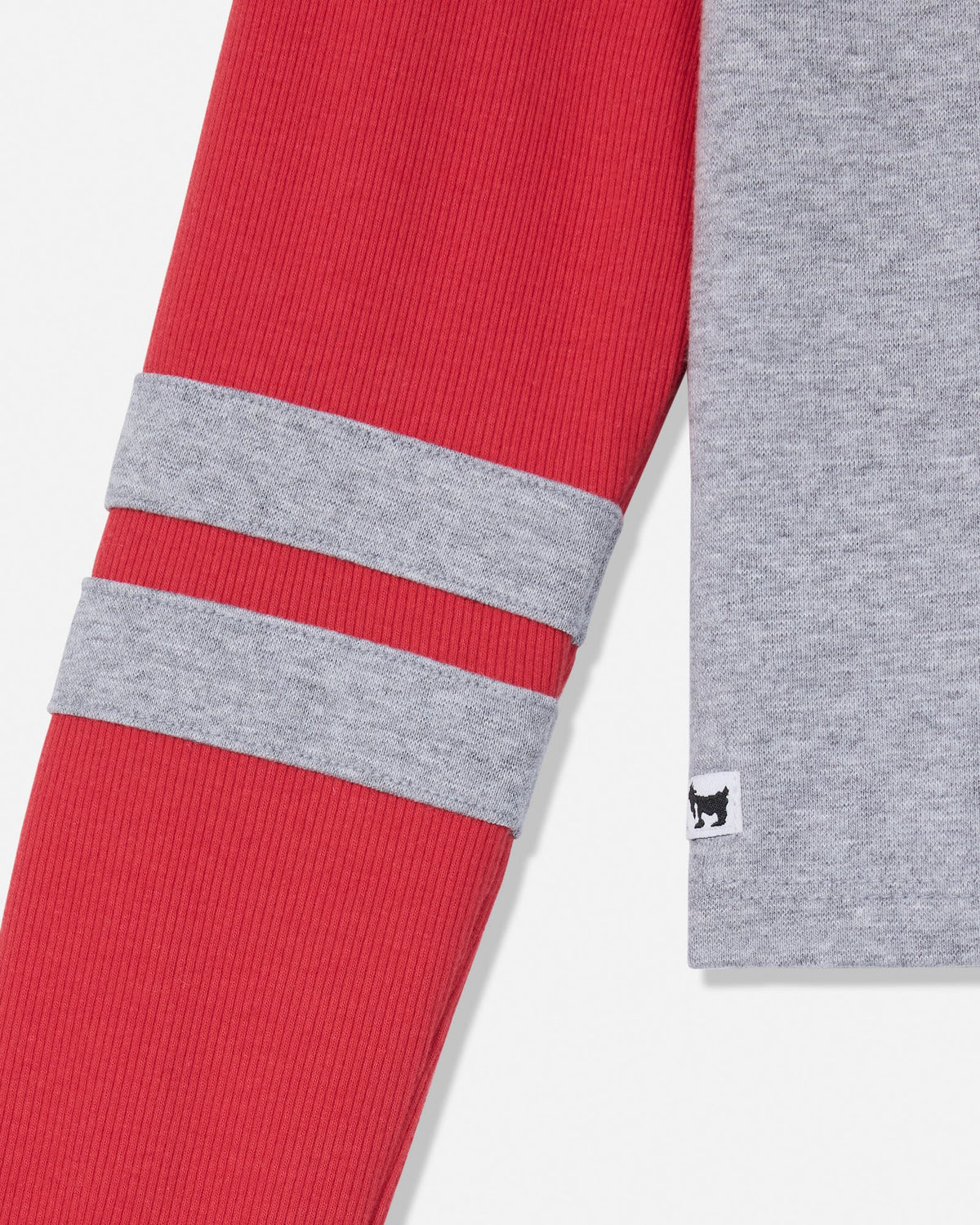 Close-up of a ribbed knit garment showing a red sleeve with two horizontal gray stripes and a heather gray cuff with a small black-and-white logo tag.