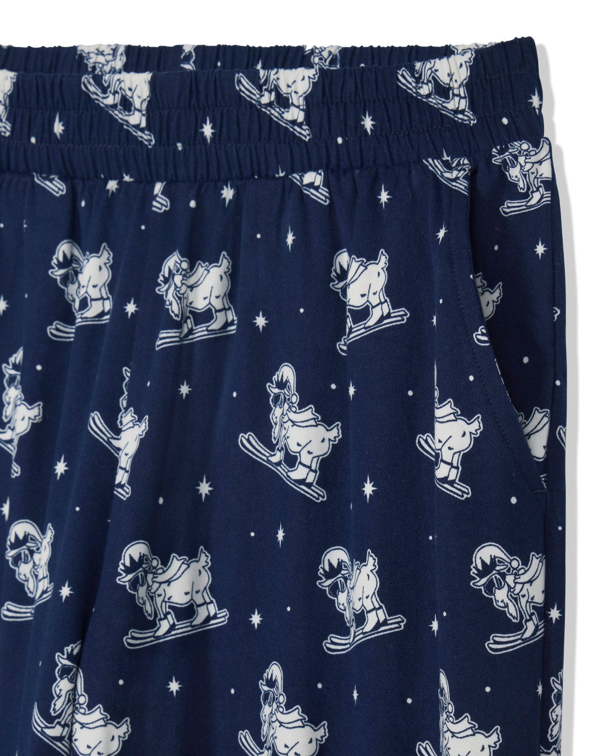 Close-up of navy blue fabric with an allover white cartoon goat skiing print and white star motifs, showing an elastic waistband.