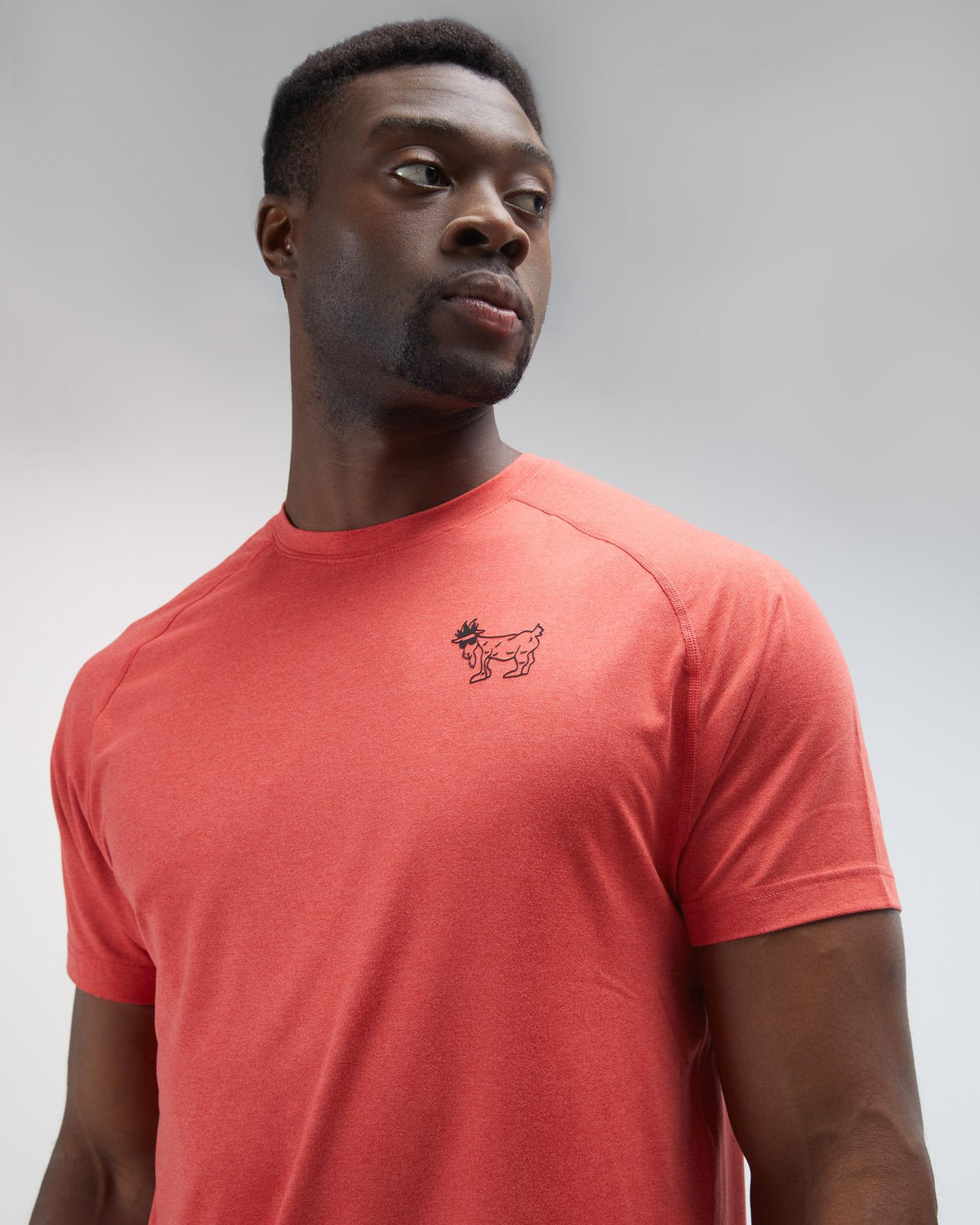 Man wearing a red t-shirt with a small logo on a gray background