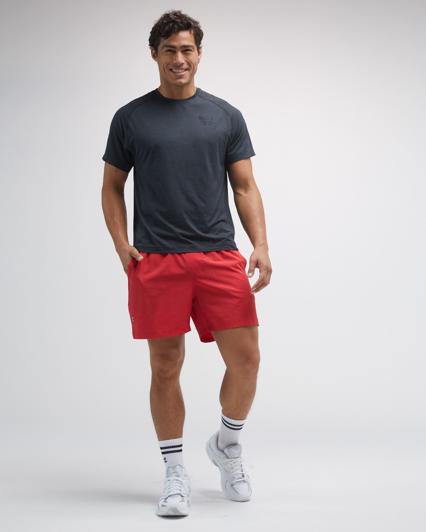Man wearing a dark gray t-shirt, red shorts, and white sneakers on a light gray background#color_black