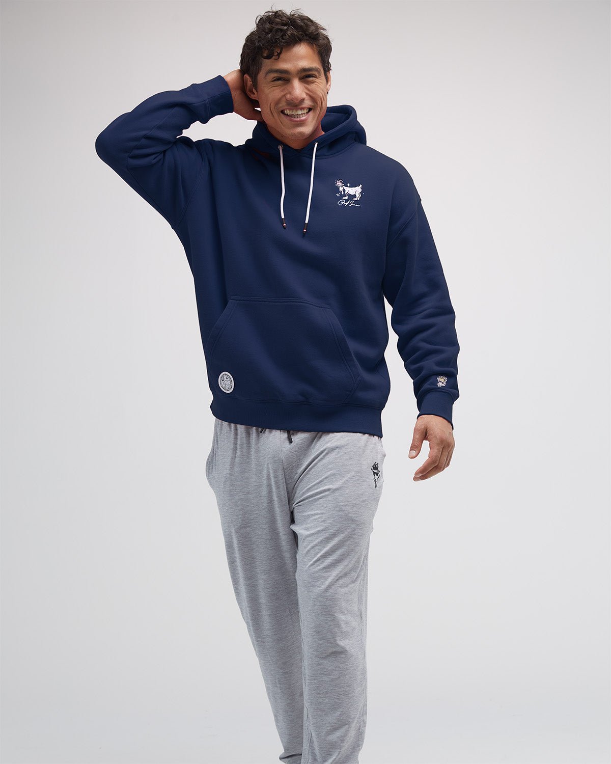 Man wearing a navy hoodie with a logo and gray pants on a white background