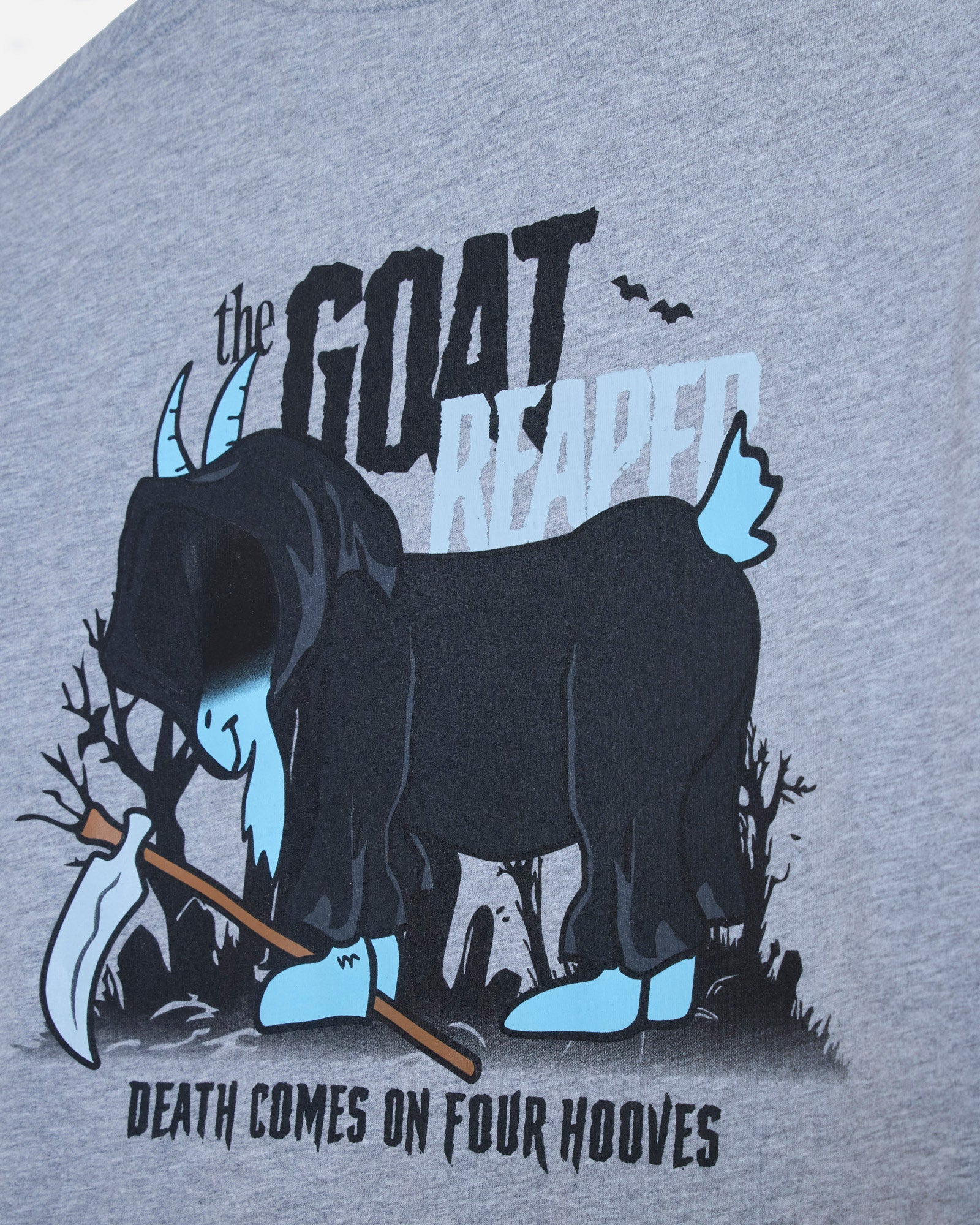 Close-up of a heather gray t-shirt featuring a graphic print of a blue goat with black cloak, holding a scythe, with the text 'the GOAT REAPER' and 'DEATH COMES ON FOUR HOOVES'.