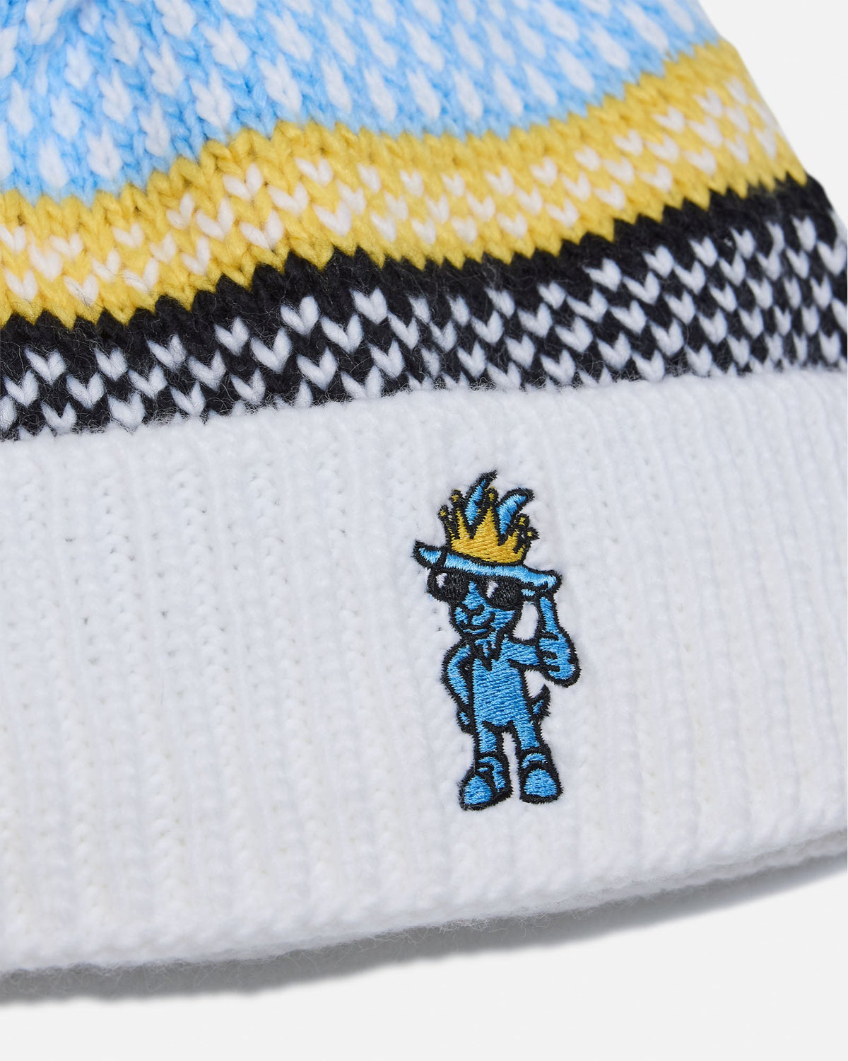 Close-up of a knit beanie with a white cuff featuring a blue cartoon character embroidered on the front, with light blue, yellow, black, and white knit bands above.