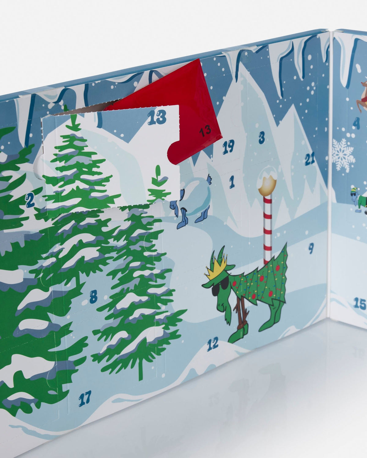 A colorful Christmas advent calendar panel showing a snowy winter scene with numbered doors and festive illustrations, including a red stocking, evergreen trees, a decorated reindeer, and snowflakes.