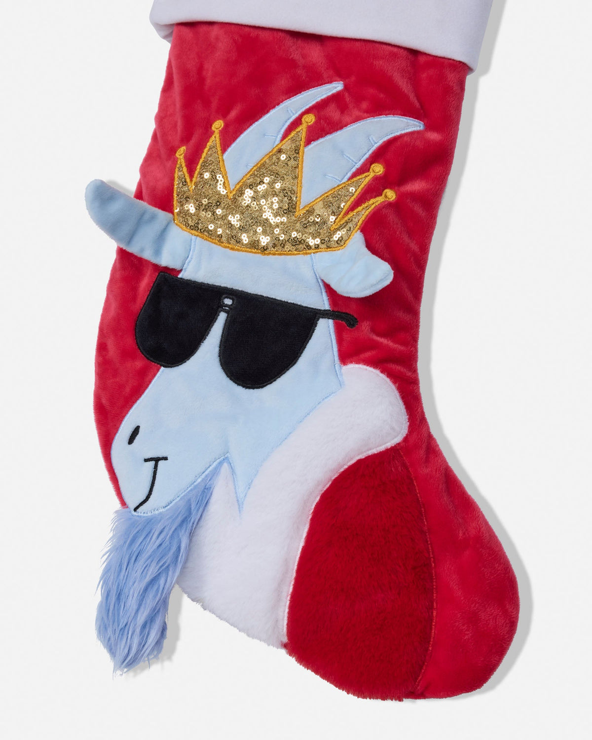 A red velvet Christmas stocking featuring a stylized blue goat character face with a gold sequined crown, black sunglasses, and a blue beard, shown against a plain white background.