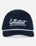 A dark navy blue corduroy baseball cap with white embroidered text reading 'The Greatest Goat USA Established 2016' on the front, featuring a white piping accent along the brim.