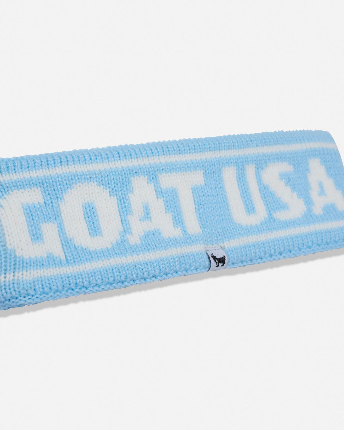 A close-up of a light blue knit headband with 'GOAT USA' knitted in white across the top, featuring a small black goat logo on the side, set against a plain white background.