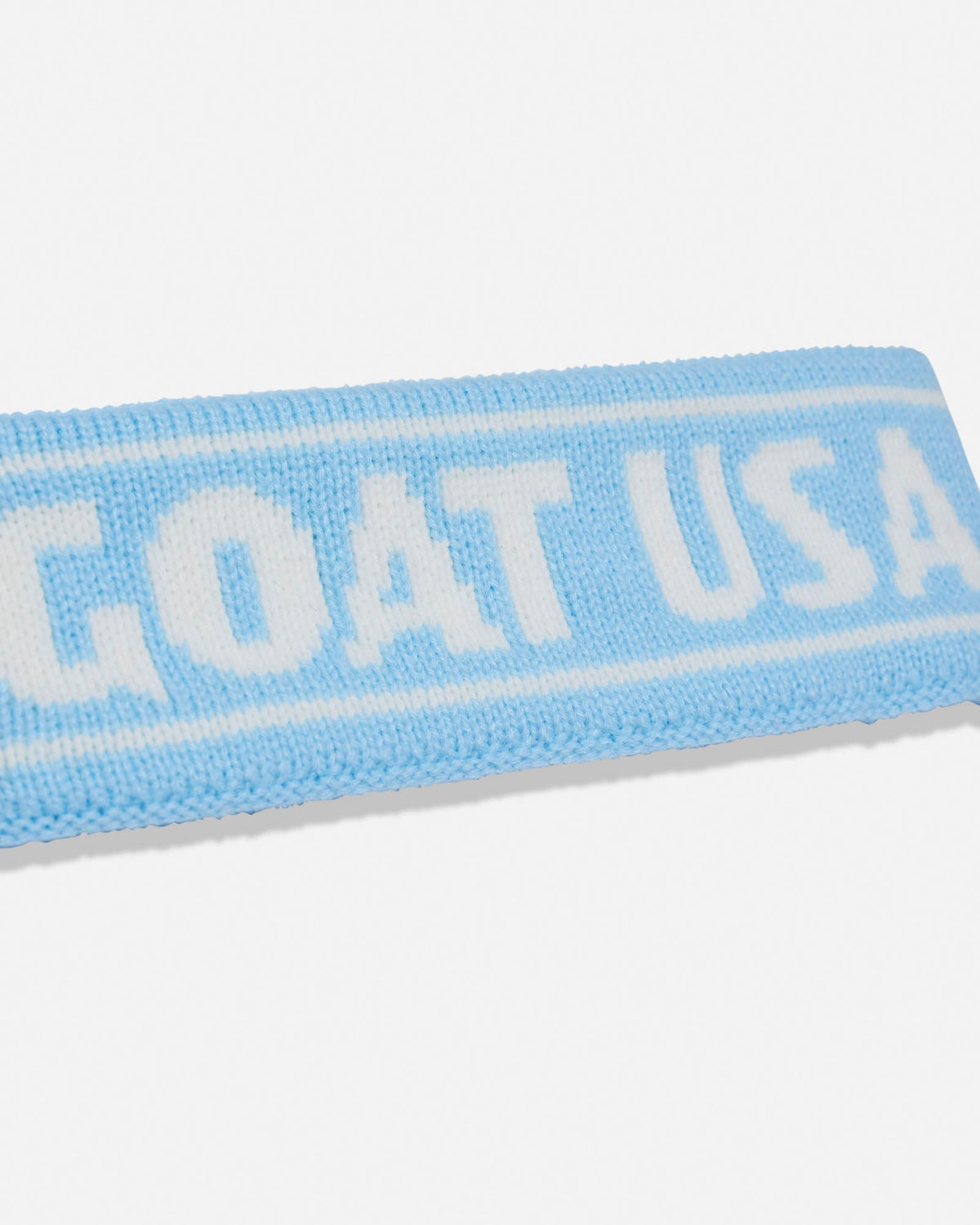 A close-up of a light blue knit headband with white lettering that reads 'GOAT USA' on a white background.