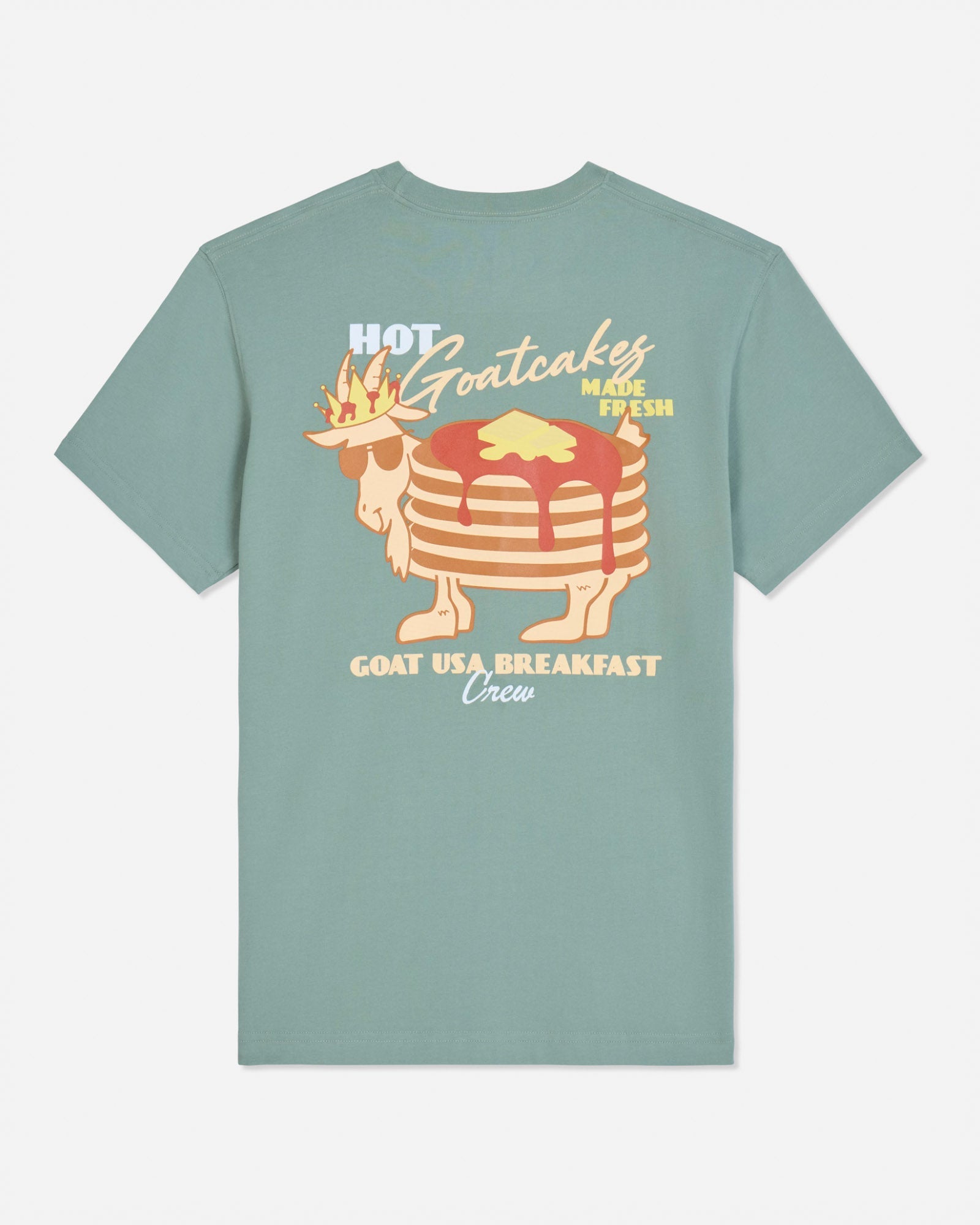 A sage green short-sleeve t-shirt with a retro graphic of a stack of pancakes wearing a crown and sunglasses, with the text 'HOT Goatcakes MADE FRESH' and 'GOAT USA BREAKFAST Union' on a light gray background.