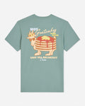 A sage green short-sleeve t-shirt with a retro graphic of a stack of pancakes wearing a crown and sunglasses, with the text 'HOT Goatcakes MADE FRESH' and 'GOAT USA BREAKFAST Union' on a light gray background.