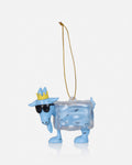 A light blue goat-shaped Christmas ornament wearing a yellow crown and black sunglasses, with a clear ice-box body containing small black snowflake details, complete with a gold hanging string, on a light gray background.