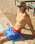 Man sitting poolside in blue and red bathing with ice pop pattern, also wearing sunglasses