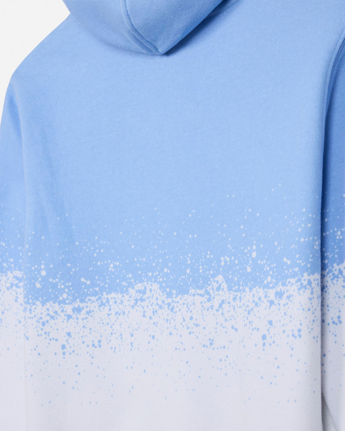 Close-up of a light blue hooded sweatshirt with a white paint-splatter gradient effect across the lower half, shown on a plain white background.