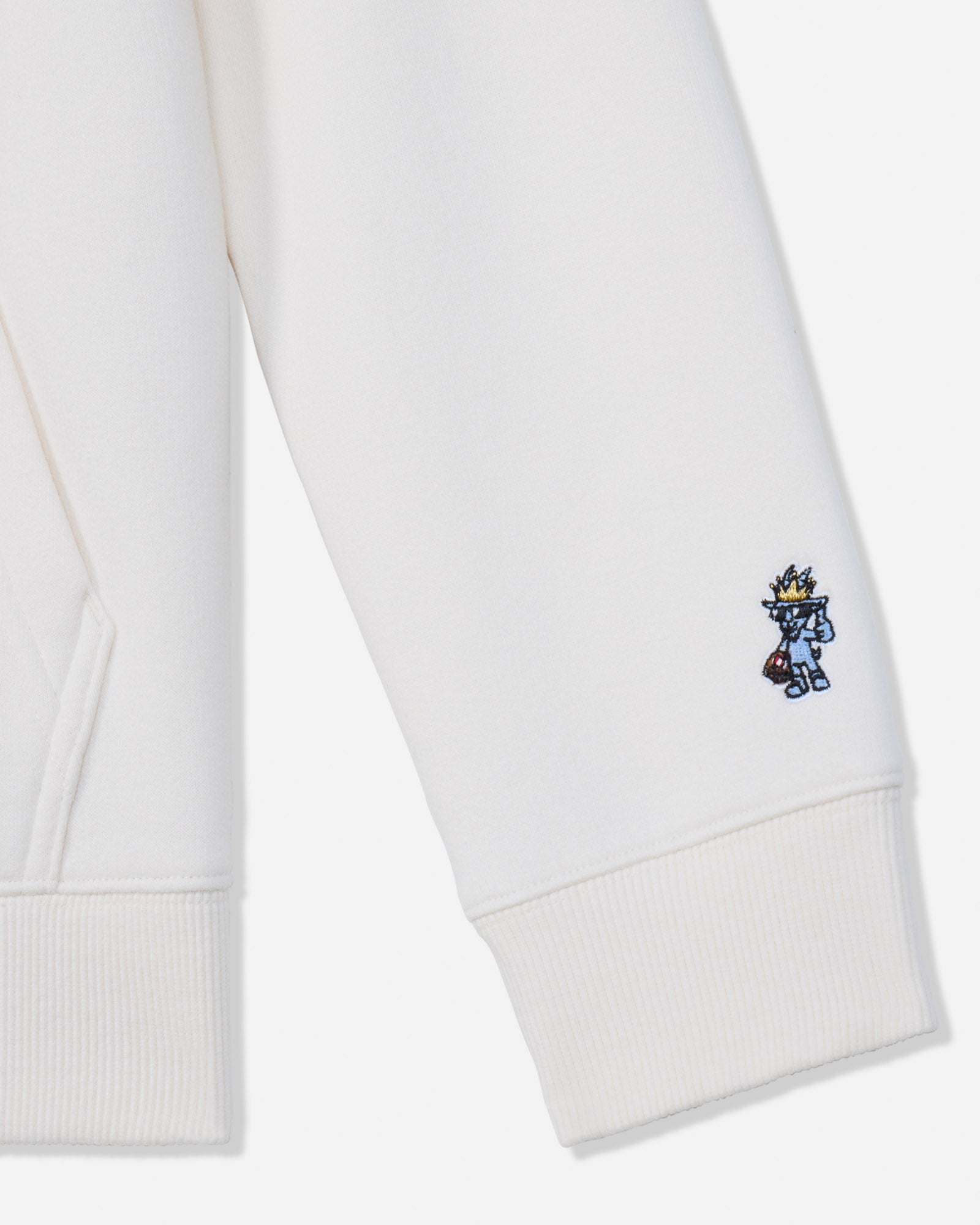 Close-up of a white ribbed cuff on a sweatshirt or hoodie, featuring a small embroidered blue and yellow character on the lower cuff.