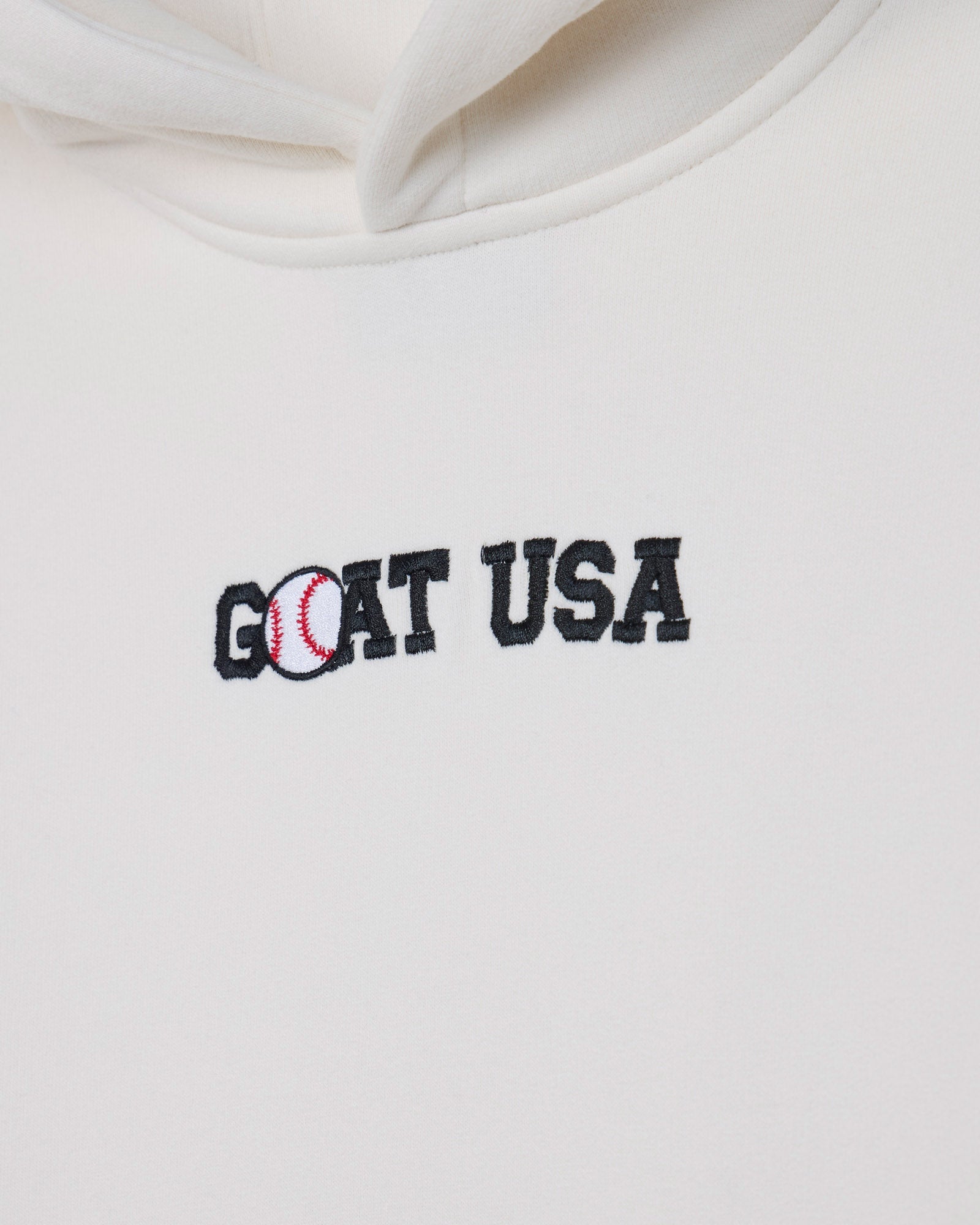Close-up of a white hoodie featuring an embroidered 'GOAT USA' logo on the chest, with the letter 'O' stylized as a baseball.