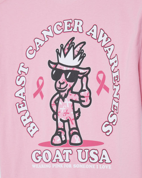 A close-up of a pink graphic t-shirt featuring a cartoon goat character wearing sunglasses and a crown, surrounded by the text 'BREAST CANCER AWARENESS' and 'GOAT USA'.