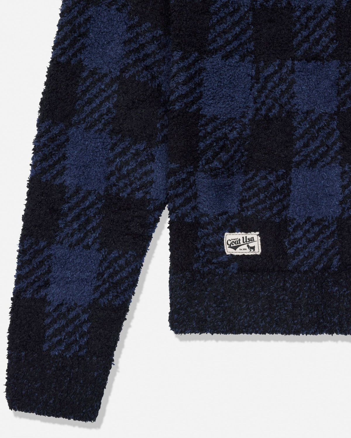 Close-up of a navy and black plaid fleece garment with a small white woven label near the lower right edge, photographed on a light gray background.