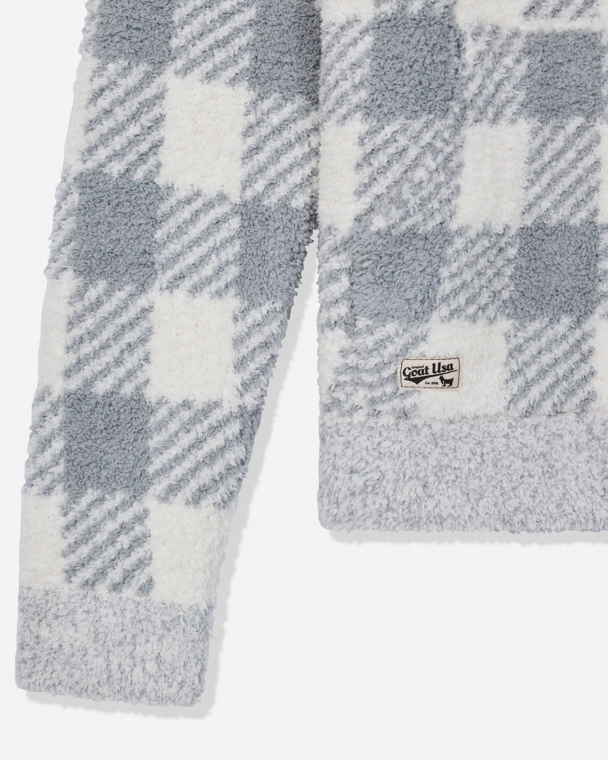 Close-up of a plush fleece garment with a gray and white buffalo plaid pattern, featuring a ribbed hem and a small visible brand patch.