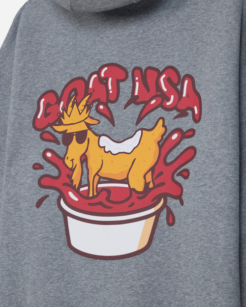 Close-up of a heather gray hoodie featuring a colorful graphic print of a yellow goat in a white cup with red splashes and the text 'GOAT USA'.