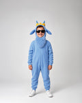 A child wearing a light blue full-body costume with a fuzzy hood, pointed ears, and a small yellow crown, standing against a plain light gray studio background.