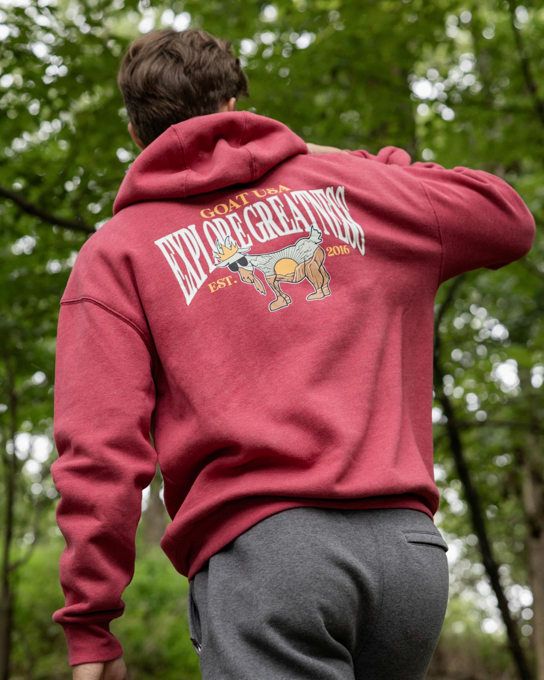 Person wearing a red hoodie with a graphic and text on the back, standing in a forest.#color_cardinal