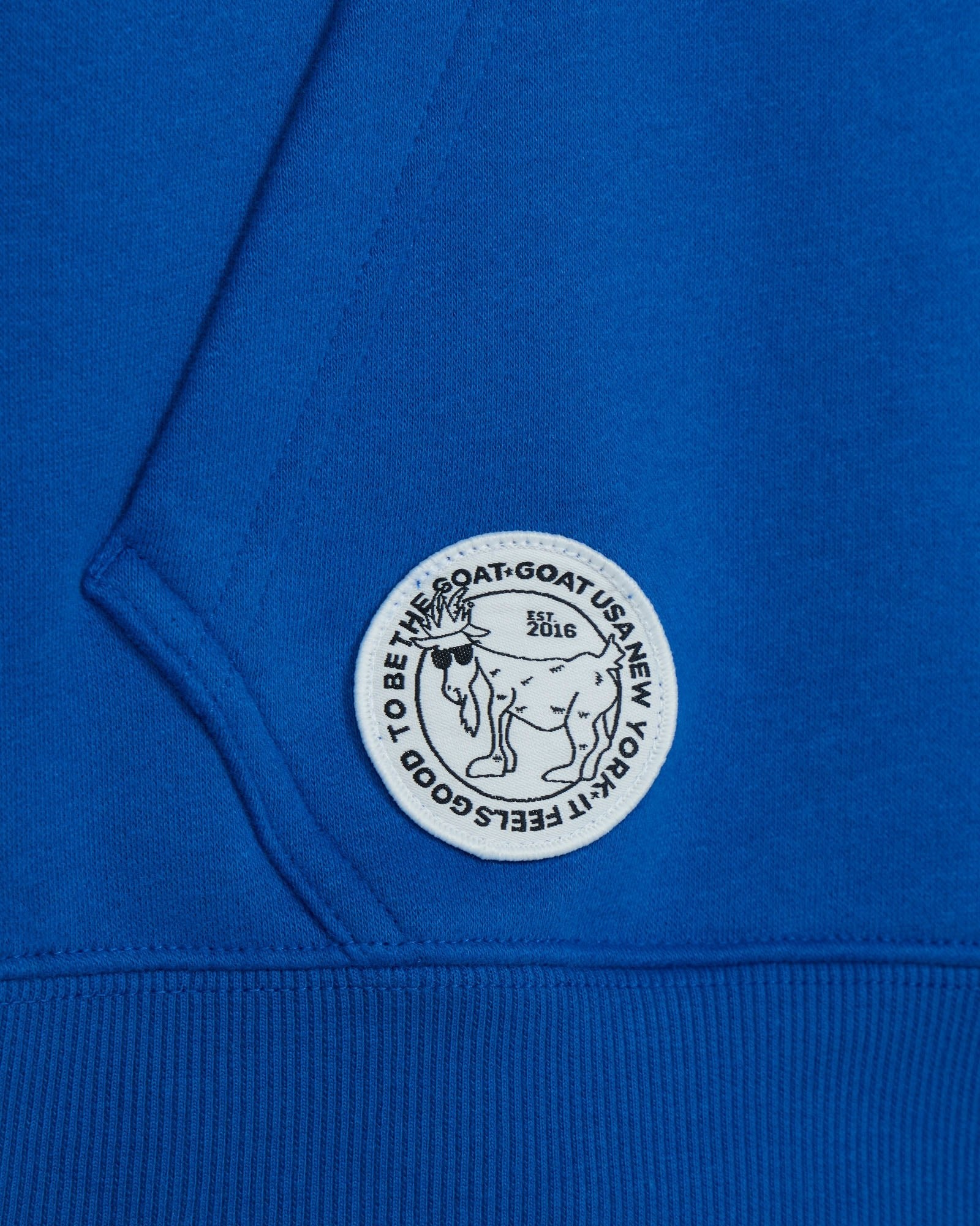 Close-up of a blue garment with a white logo featuring text and a goat illustration.