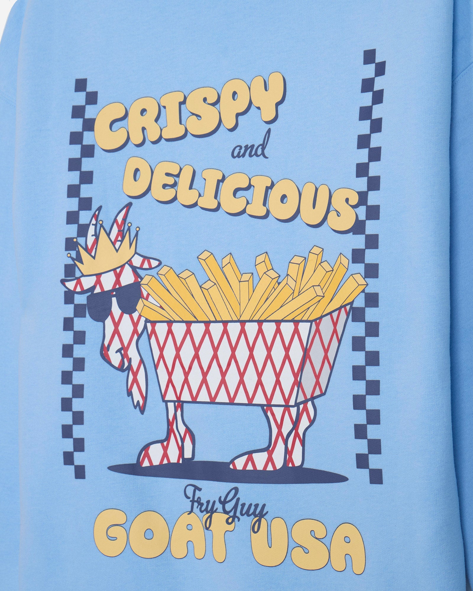 A close-up of a light blue graphic t-shirt featuring a stylized red and white patterned goat wearing sunglasses and a crown, filled with yellow french fries. The text reads 'CRISPY and DELICIOUS' and 'FryGuy GOAT USA'.