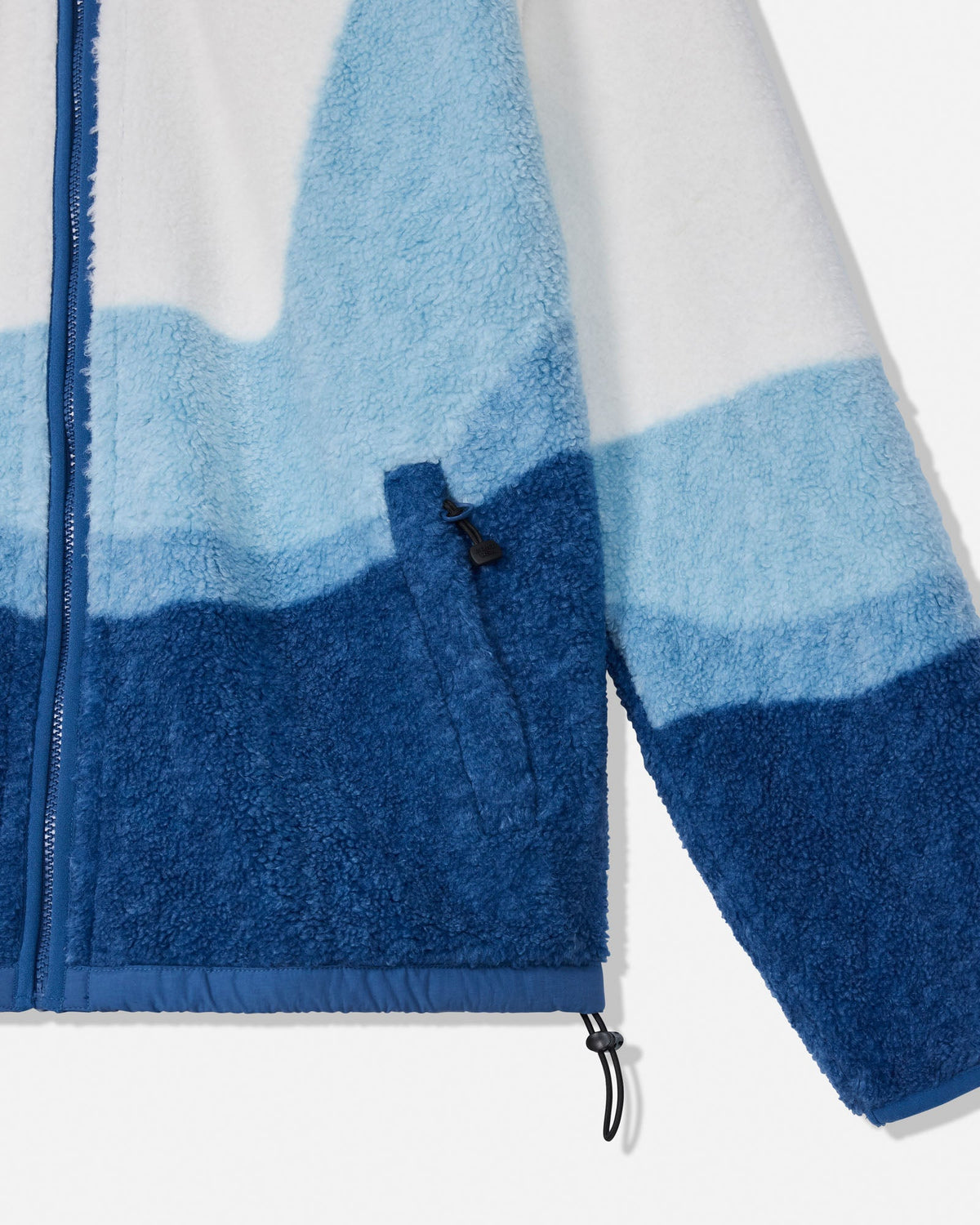 Close-up of a fleece zip jacket with a blue and white wavy mountain-patterned design, showing the textured fabric, zipper, and drawcord details.
