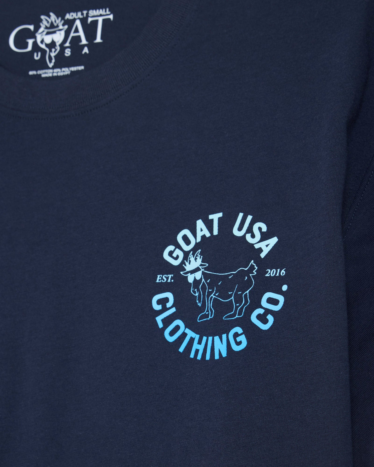 Close-up of a navy blue t-shirt featuring a light blue and white circular 'GOAT USA CLOTHING CO.' graphic on the chest, with the brand's logo printed inside the collar.