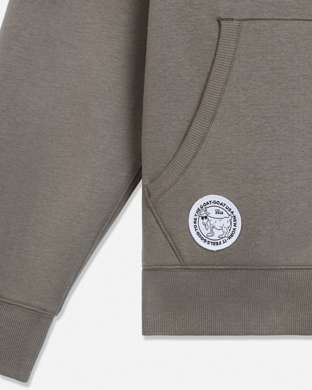 Close-up of a heather taupe sweatshirt sleeve with a circular white and black  patch on the cuff, set against a clean white background.#color_smokey-olive