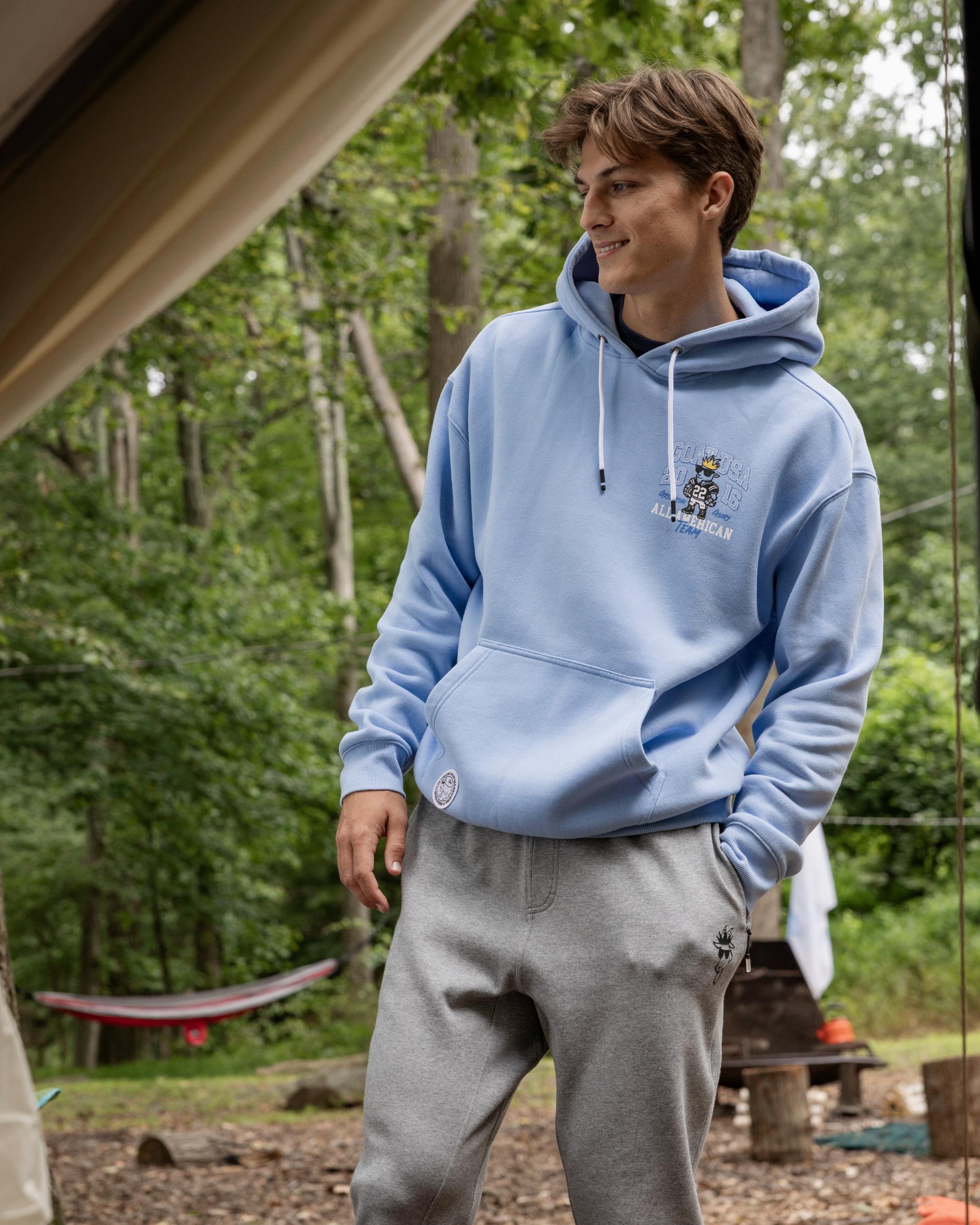 Person wearing a light blue hoodie with a logo in a forest setting