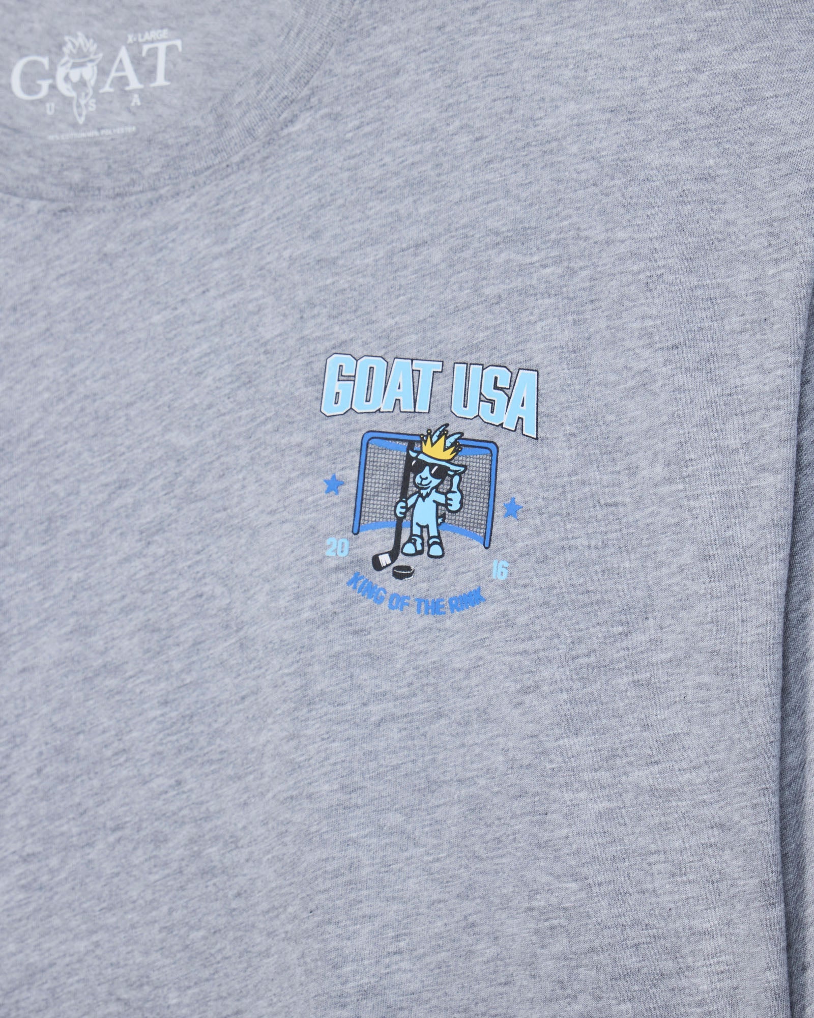 Close-up of a heather gray t-shirt featuring a 'GOAT USA' graphic on the chest with a cartoon hockey goat character and the text 'King of the Rink'.