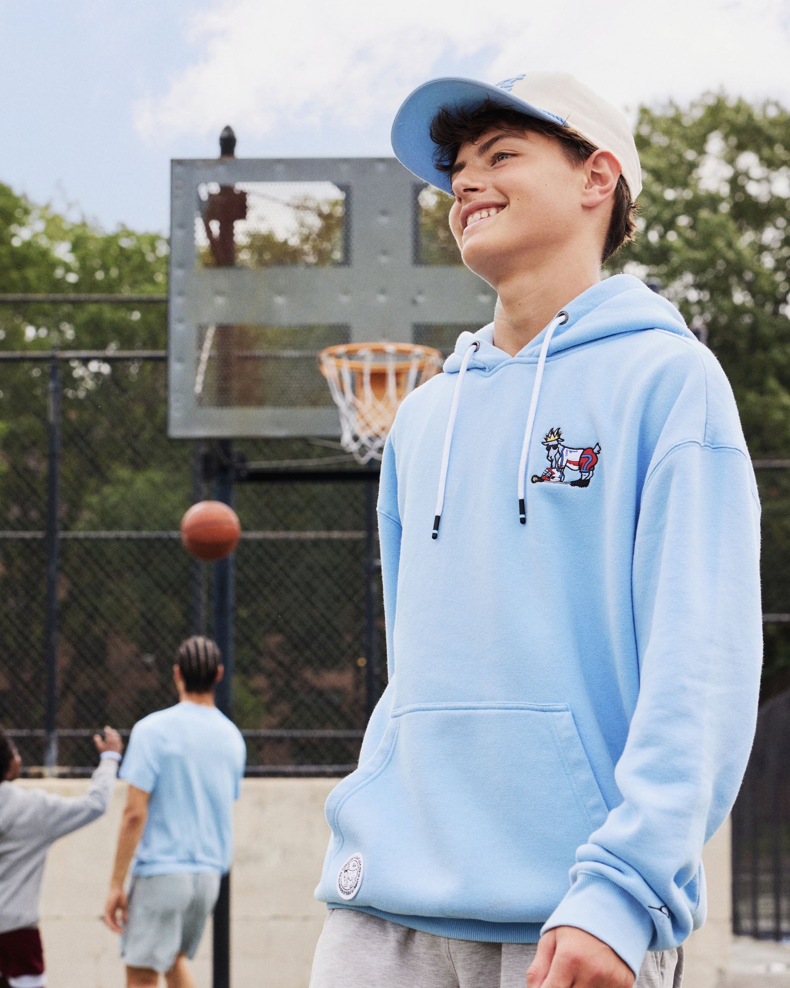 Person wearing a light blue hoodie with a lacrosse player goat on a basketball court