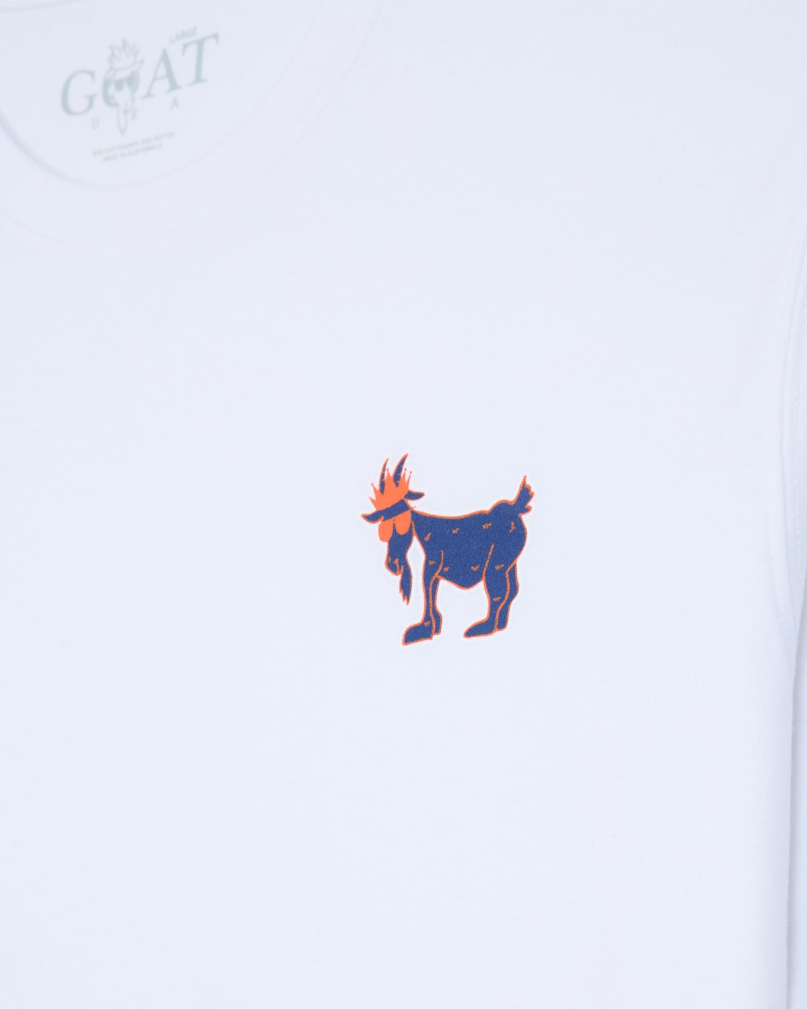 A close-up of a white t-shirt featuring a small central graphic of a stylized goat in navy blue with orange accents, and a faint circular 'GOAT' logo printed in the upper left corner.