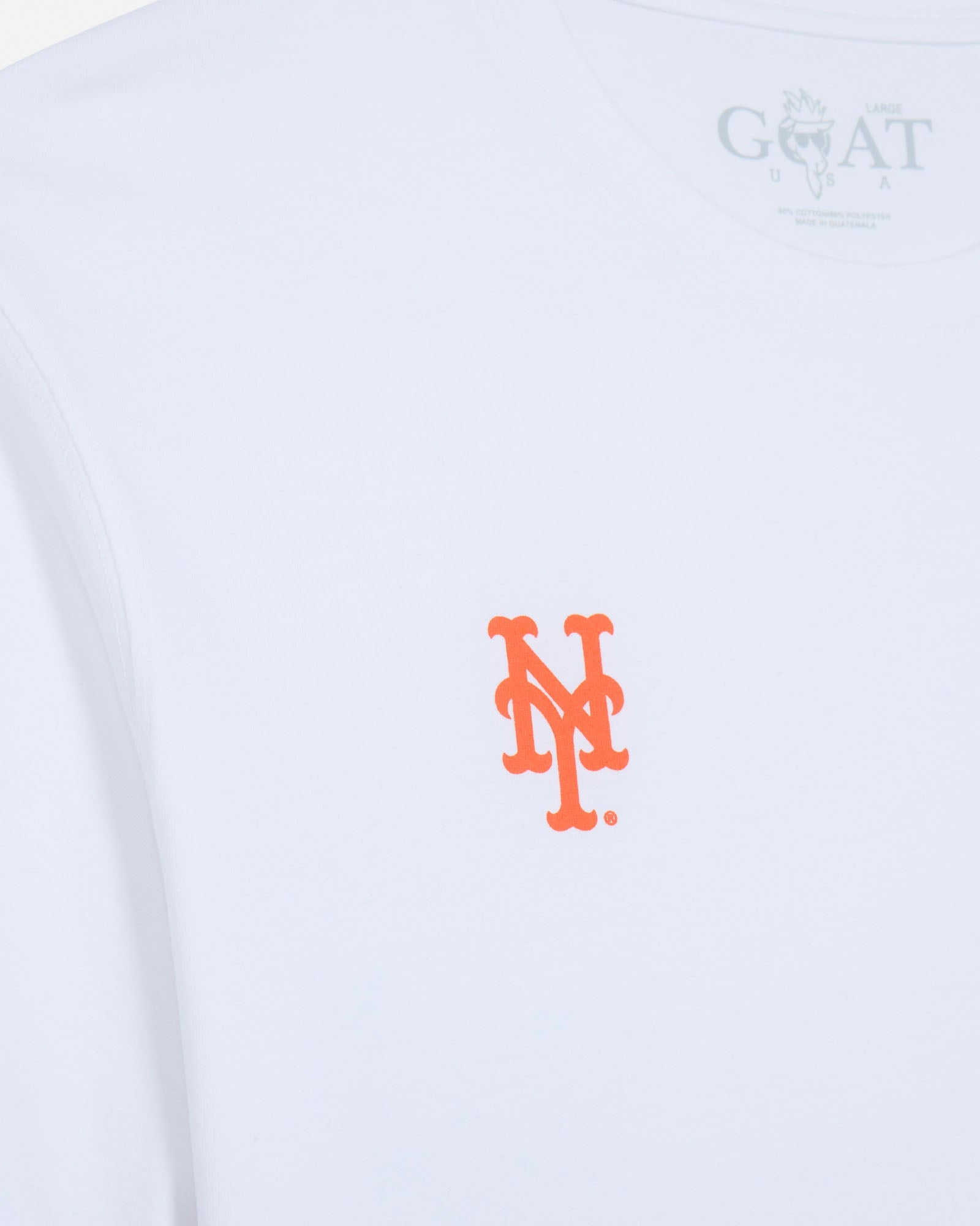 Close-up of a white long-sleeve t-shirt featuring a bright orange embroidered 'NY' logo on the center chest and a gray 'GOAT USA' brand print inside the collar.