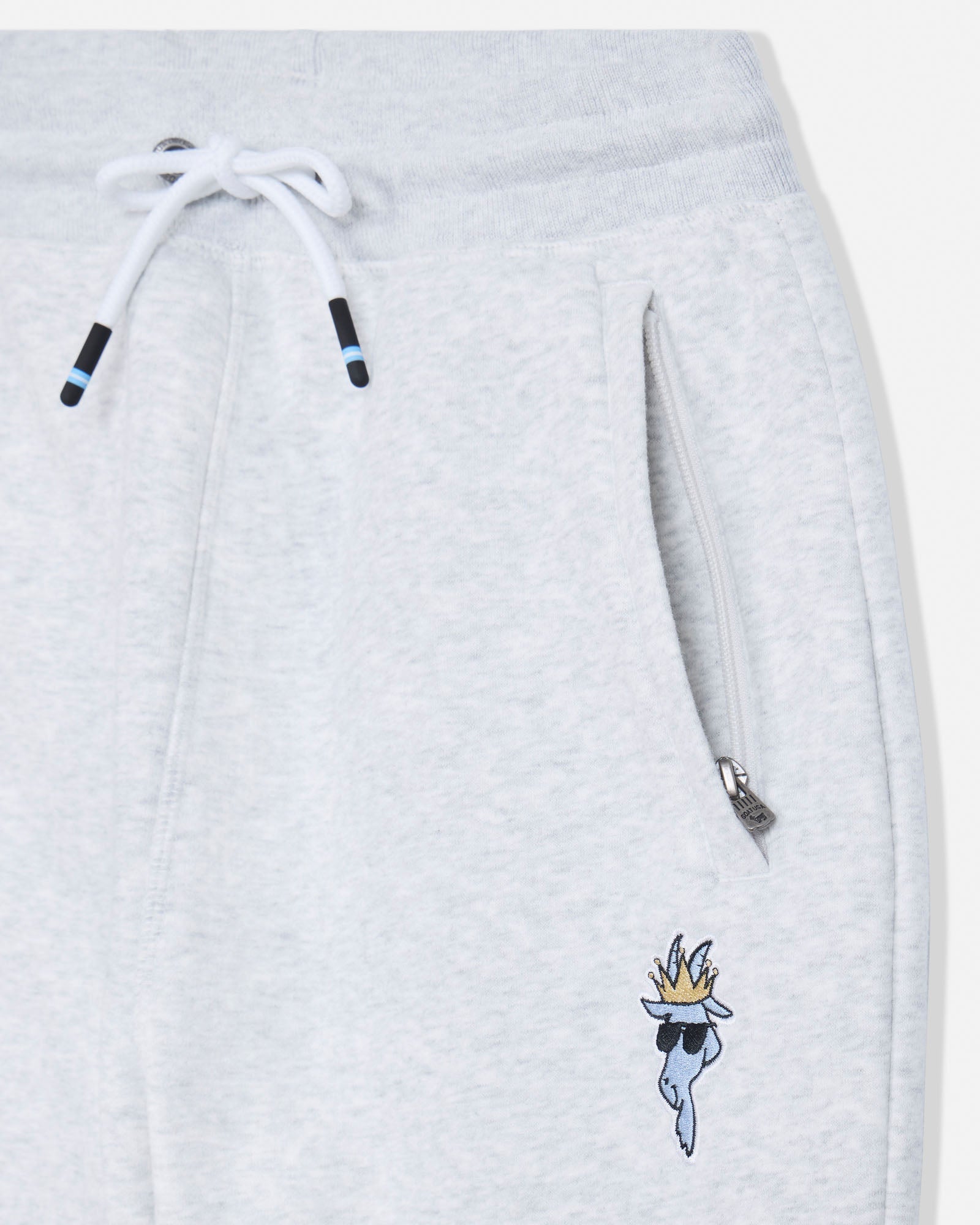 Close-up of light heather gray sweatpants showing the drawstring, zippered pocket, and a small embroidered flaming character logo near the lower left leg.#color_pale-gray