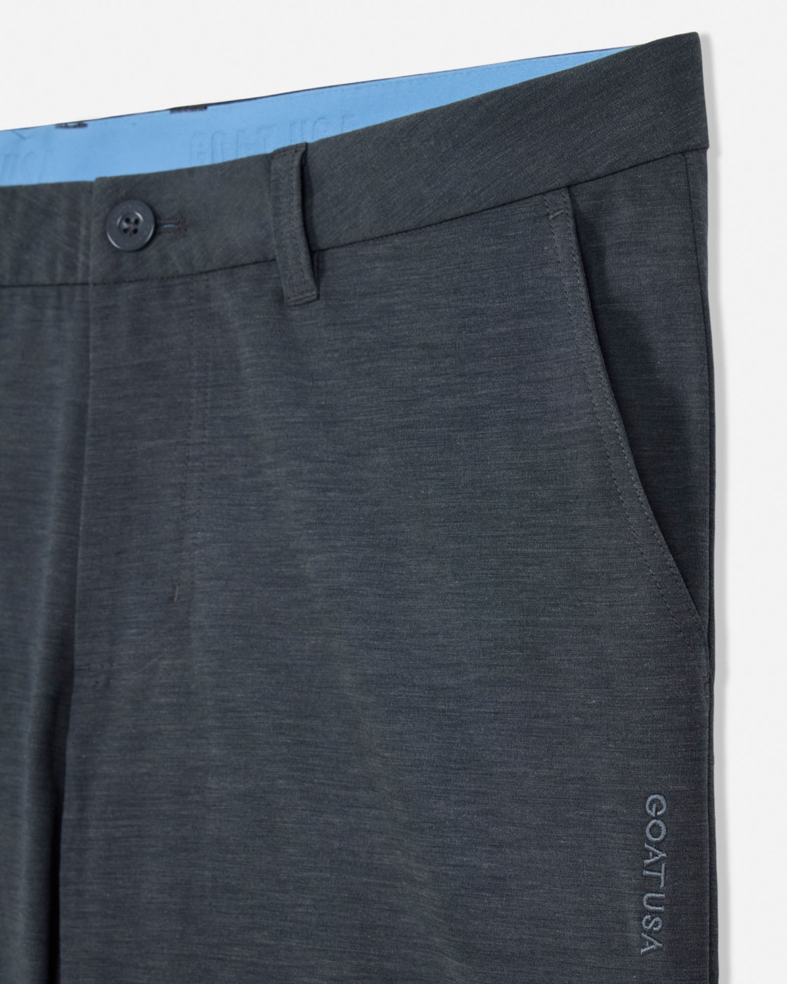 Close-up of dark gray pants with a button and waistband detail, brand 'GOAT USA' visible.#color_gray
