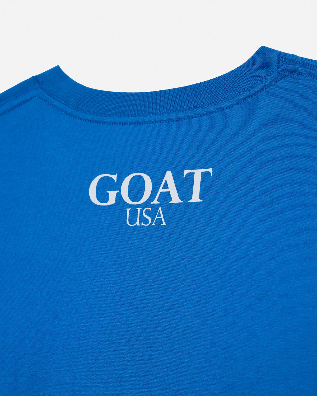Close-up of the back of a bright blue t-shirt with 'GOAT USA' printed in white serif text on the center.