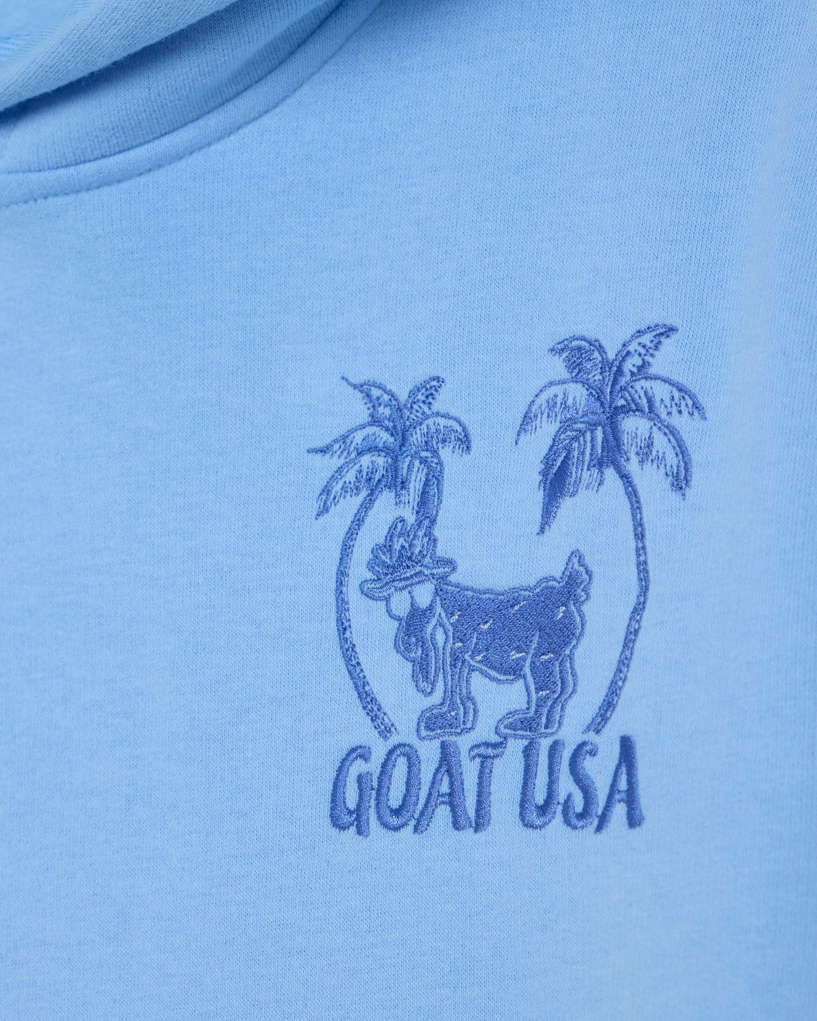 Blue t-shirt with 'GOAT USA' logo featuring a goat and palm trees on a light blue background.#color_carolina-blue