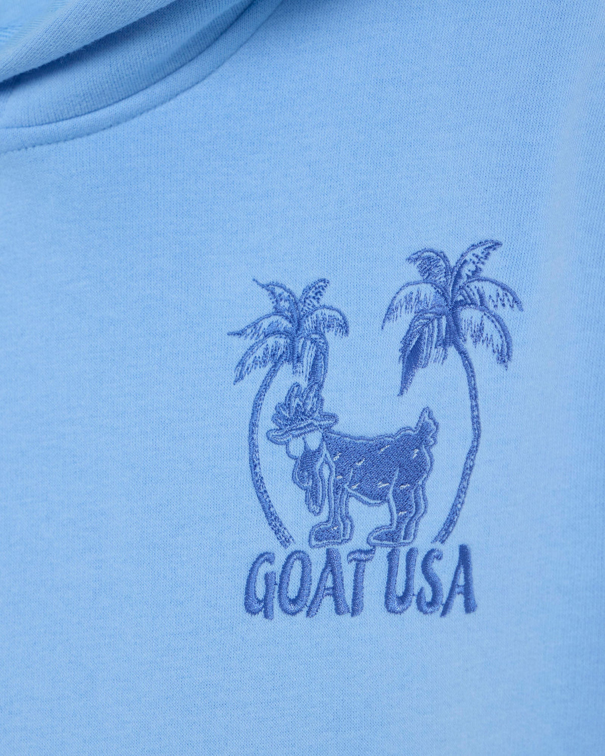 Blue t-shirt with 'GOAT USA' logo featuring a goat and palm trees on a light blue background.