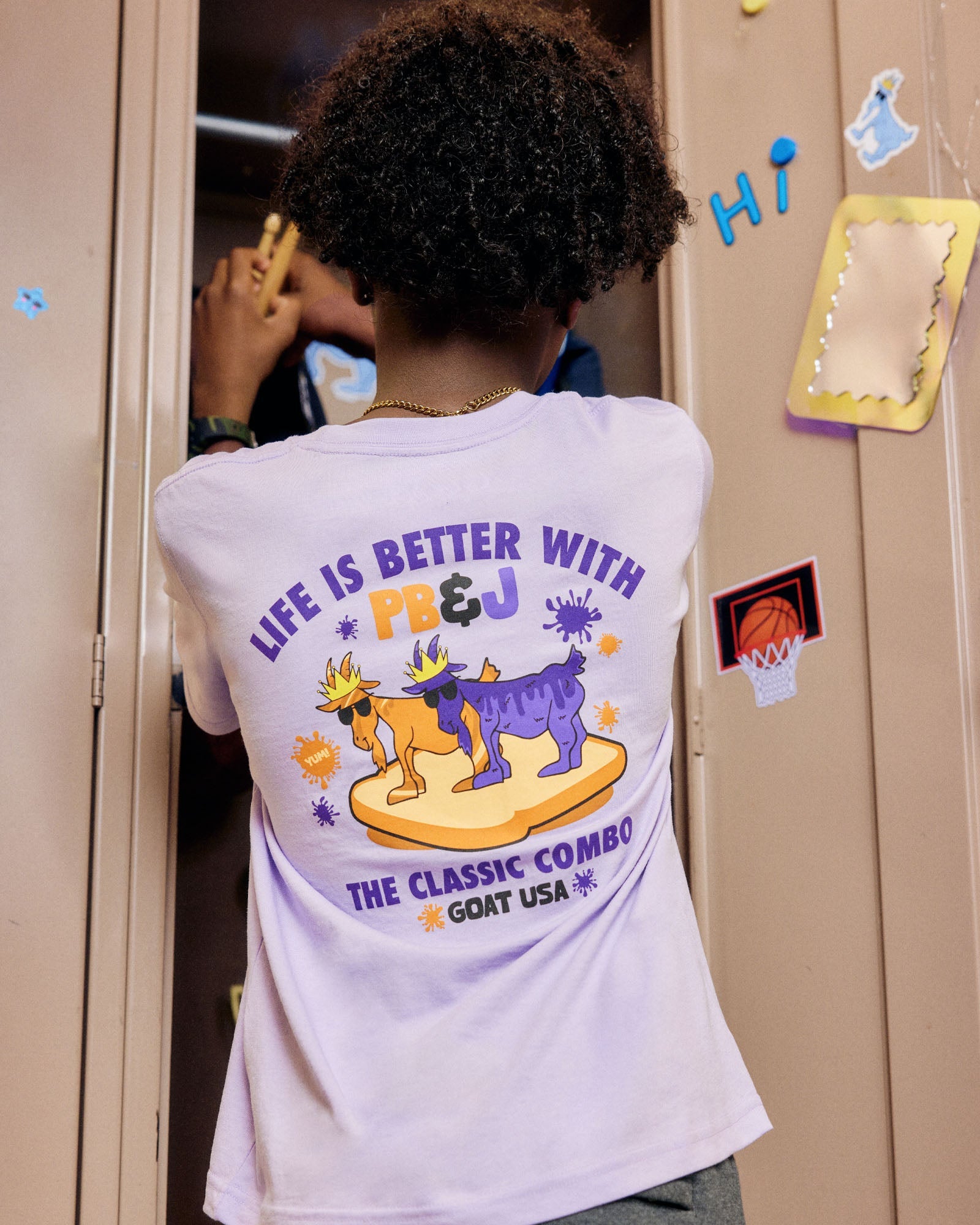 Person wearing a t-shirt with a graphic design and text, standing in front of a locker.