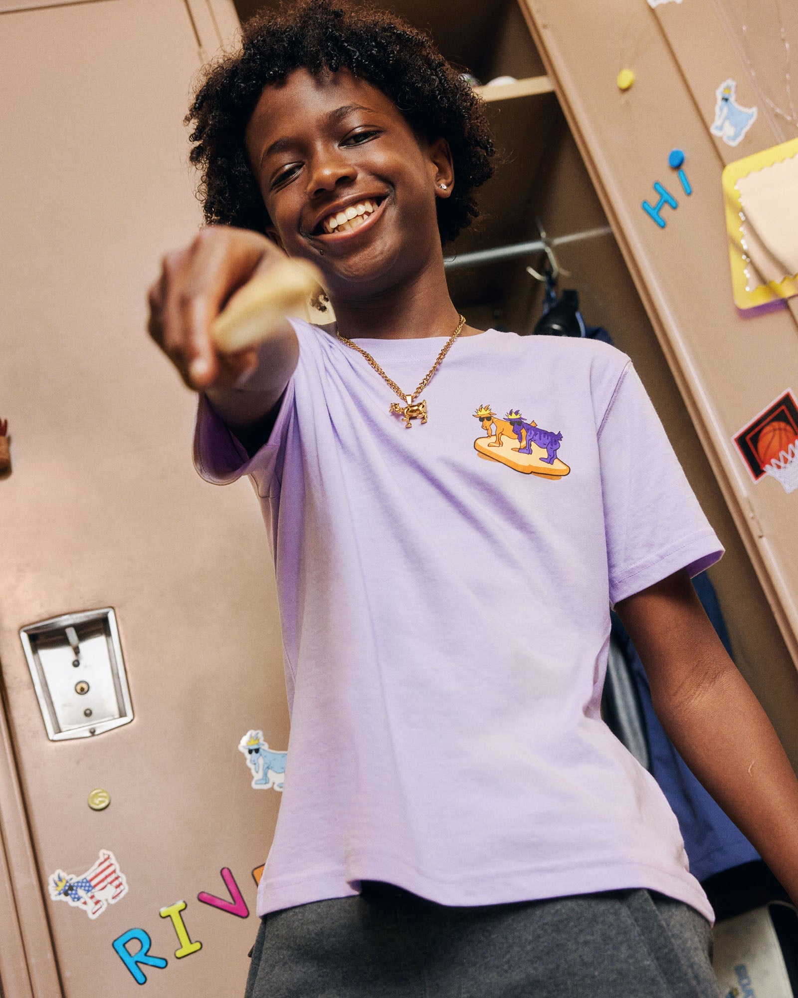 Child wearing a purple t-shirt with a logo, standing in front of lockers with colorful stickers.